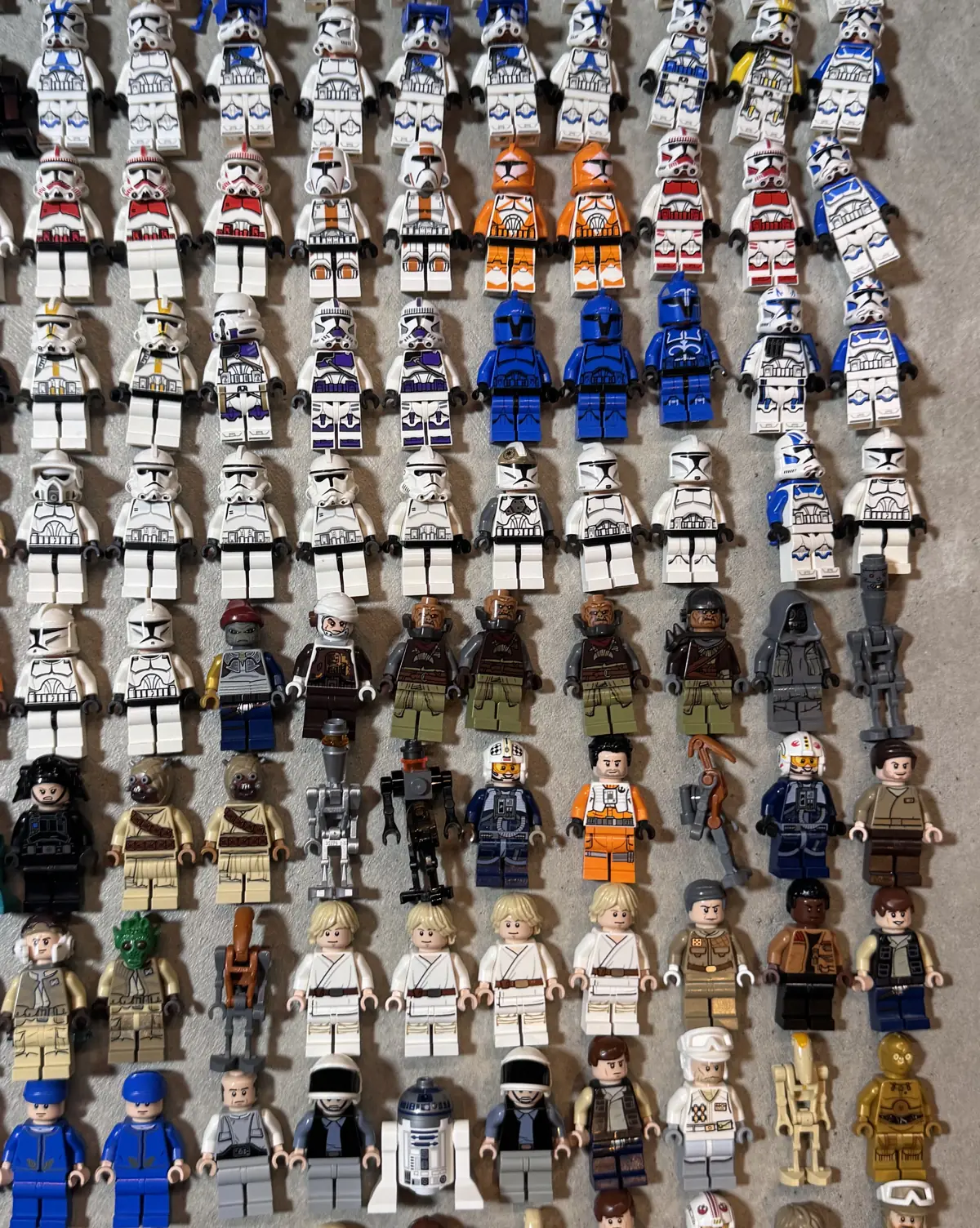A lot of 80 Star Wars LEGO minifigures laid out in rows on a grey carpet